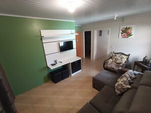Ein Wohnzimmer mit Fernseher, einer Couch und einem gemusterten Sessel.