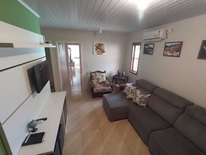 Un salon comprenant un canapé, un fauteuil, une petite table et un téléviseur fixé au mur.