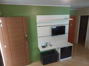 Ein Zimmer mit einem an einer weißen Kommode befestigten Fernseher, einem kleinen Tisch mit einer Globus und Fernbedienungen sowie einer braunen Tür.