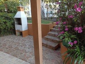 Un pati amb paviment de pedra, un barbacoa i una escala cap a una zona coberta.