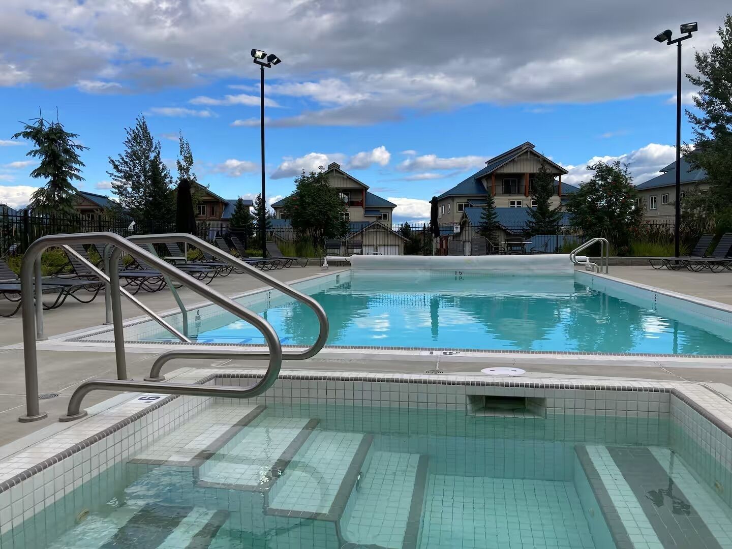 A swimming pool with tiled edges, a metal ladder, and lounge chairs.
