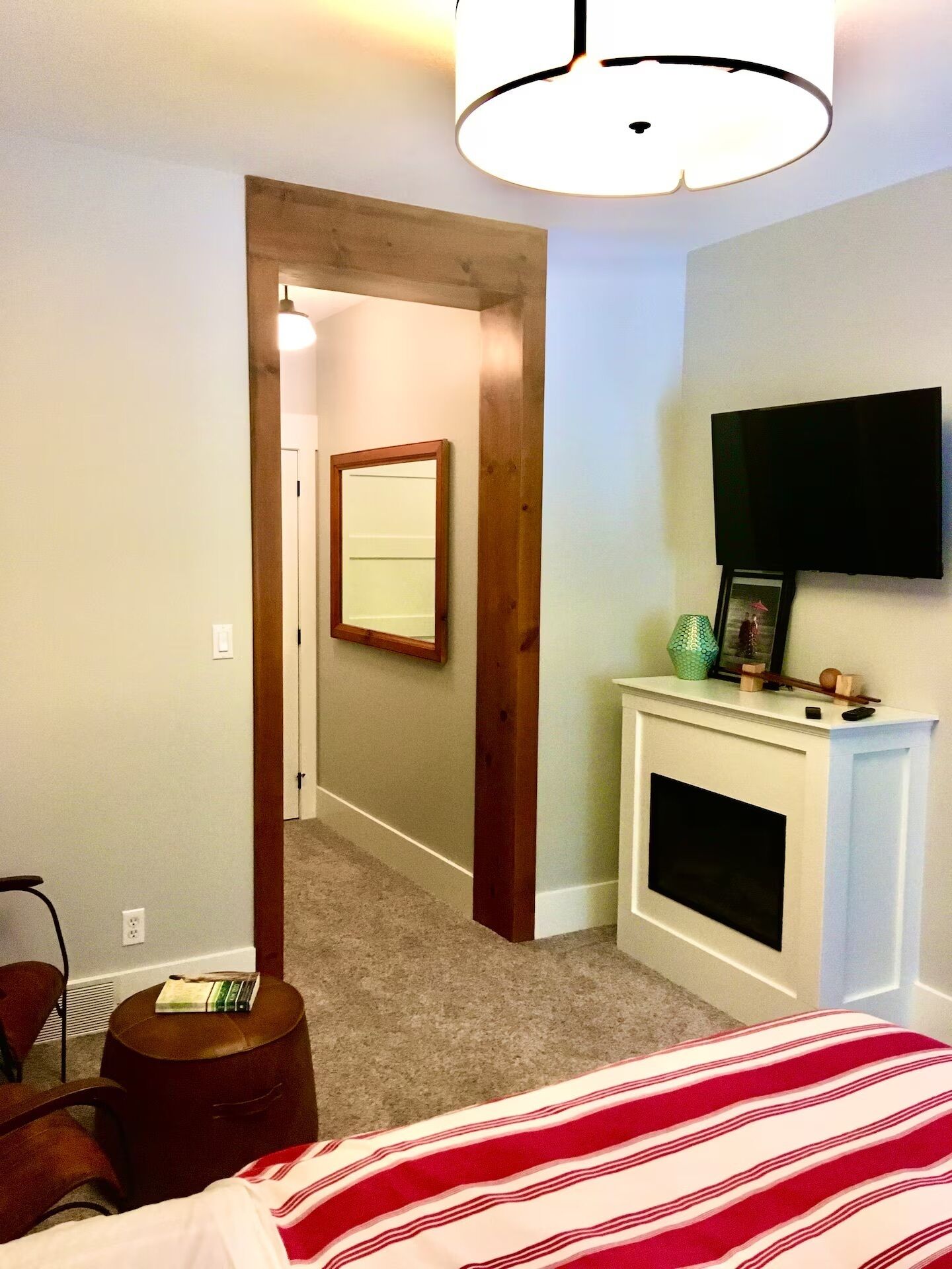 A bedroom with a bed, a television mounted above a fireplace, a mirror on the wall, and a door leading to another room.