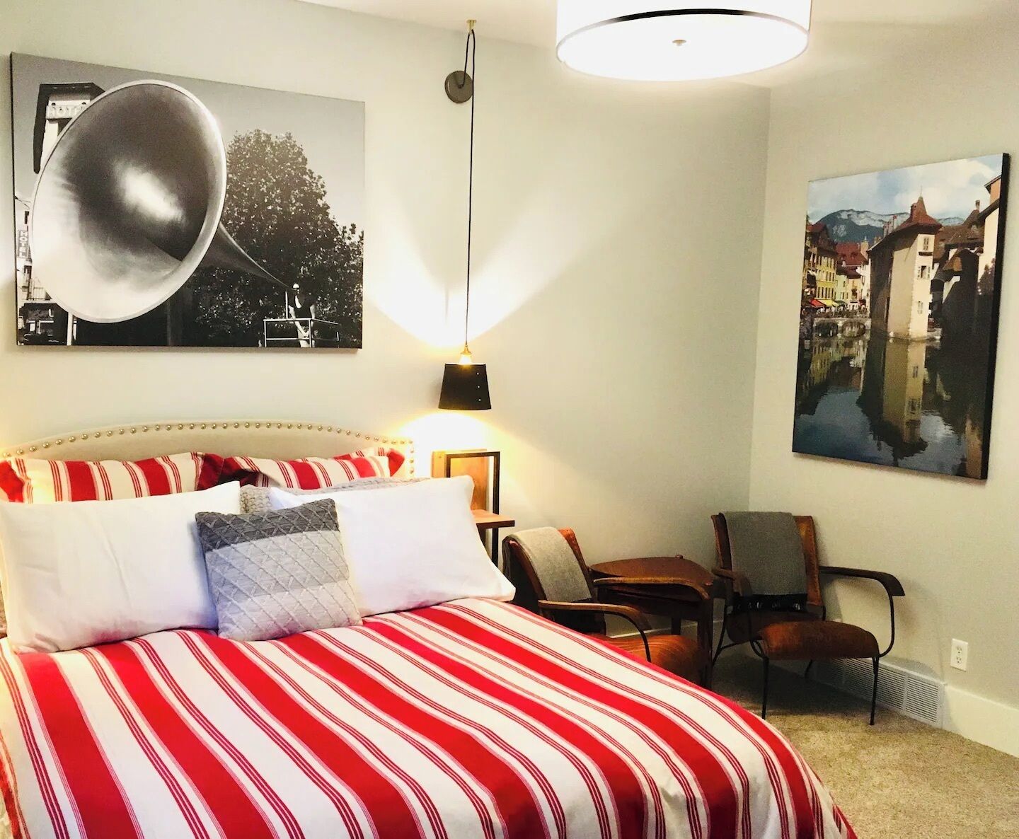 A bedroom with a bed, a chair, a lamp, and two wall-mounted pictures.