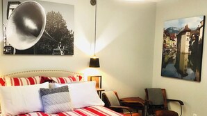 Et soveværelse med en seng, en stol, en lampe og to billeder hængende på væggen.