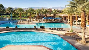 A large outdoor swimming pool with multiple sections, surrounded by palm trees and lounge chairs.