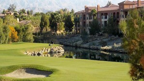 A golf course with a pond, a building with a red roof, and mountains in the background.