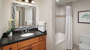 A bathroom with a granite countertop sink, wooden cabinets, a large mirror with a mosaic frame, a white toilet, and a shower with a white curtain.