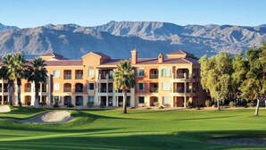 A multi-story hotel with a golf course in front, surrounded by mountains.