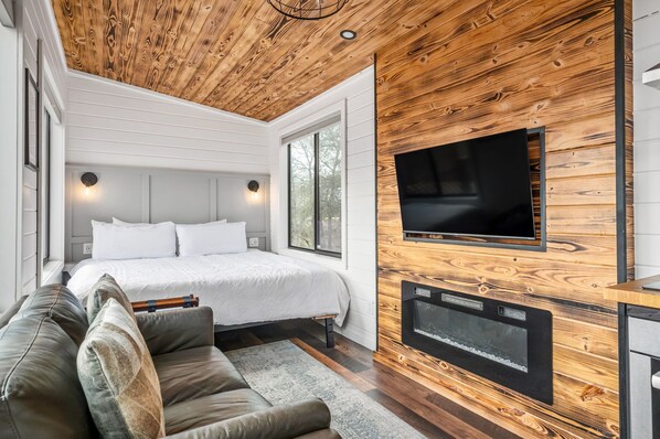 Une chambre moderne avec un grand lit, un téléviseur fixé à un mur en bois et un coin salon confortable avec un canapé.