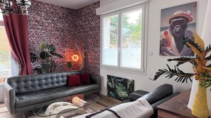 A living room with a brick wall, a sofa, a glass coffee table, and a large window. - Vrbo Property (La Tranche-sur-Mer)