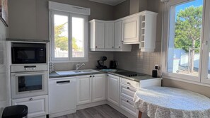 A kitchen with white cabinets, a microwave, a sink, and a window with a view of trees. - Cozy house with a private hot tub, 80 m from the ocean, 200 m from downtown, parking available (La Tranche-sur-Mer)