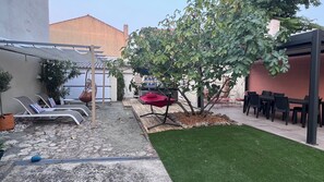 A patio area with lounge chairs, a red umbrella, and a small tree. - Vrbo Property (La Tranche-sur-Mer)