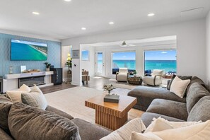 Ein großzügiges Wohnzimmer mit einem großen Fernseher, bequemen Sitzgelegenheiten und Blick auf den Ozean.