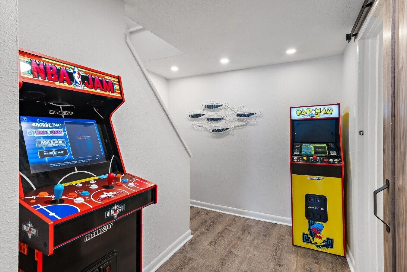 Eine Indoor-Spielhalle mit zwei Basketball-Spielautomaten, einer mit der Aufschrift 'NBA JAM' und der andere mit 'PAC-MAN'.