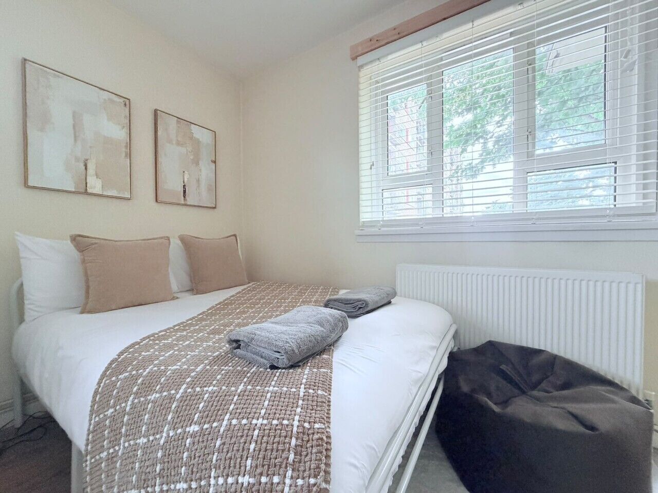 A bedroom with a bed, pillows, a blanket, a radiator, and a window with blinds.