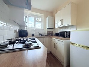 A kitchen with a gas stove, microwave, and white cabinets. - White Oak Studio Hideaway (London)