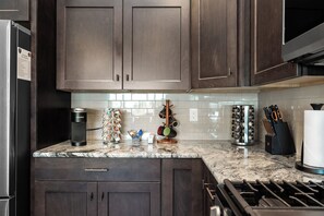 A kitchen with dark wood cabinets, a stainless steel range hood, a coffee maker, and various kitchen utensils. - Cozy Cove - Hot Tub, Waterfront, Game Room Sleeps 6 (Ocean Shores)