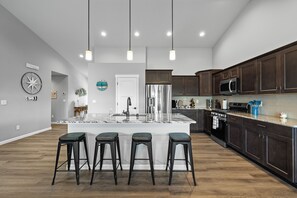 A modern kitchen with a central island, bar stools, stainless steel appliances, and dark wood cabinets. - Cozy Cove - Hot Tub, Waterfront, Game Room Sleeps 6 (Ocean Shores)