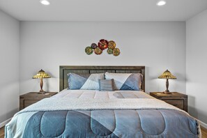 A bedroom with a large bed, two bedside tables with lamps, a wooden headboard, and a wall decoration. - Cozy Cove - Hot Tub, Waterfront, Game Room Sleeps 6 (Ocean Shores)