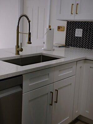 A kitchen with a stainless steel sink, white cabinetry, and a black and white herringbone backsplash. - The Sailfish (Stuart)