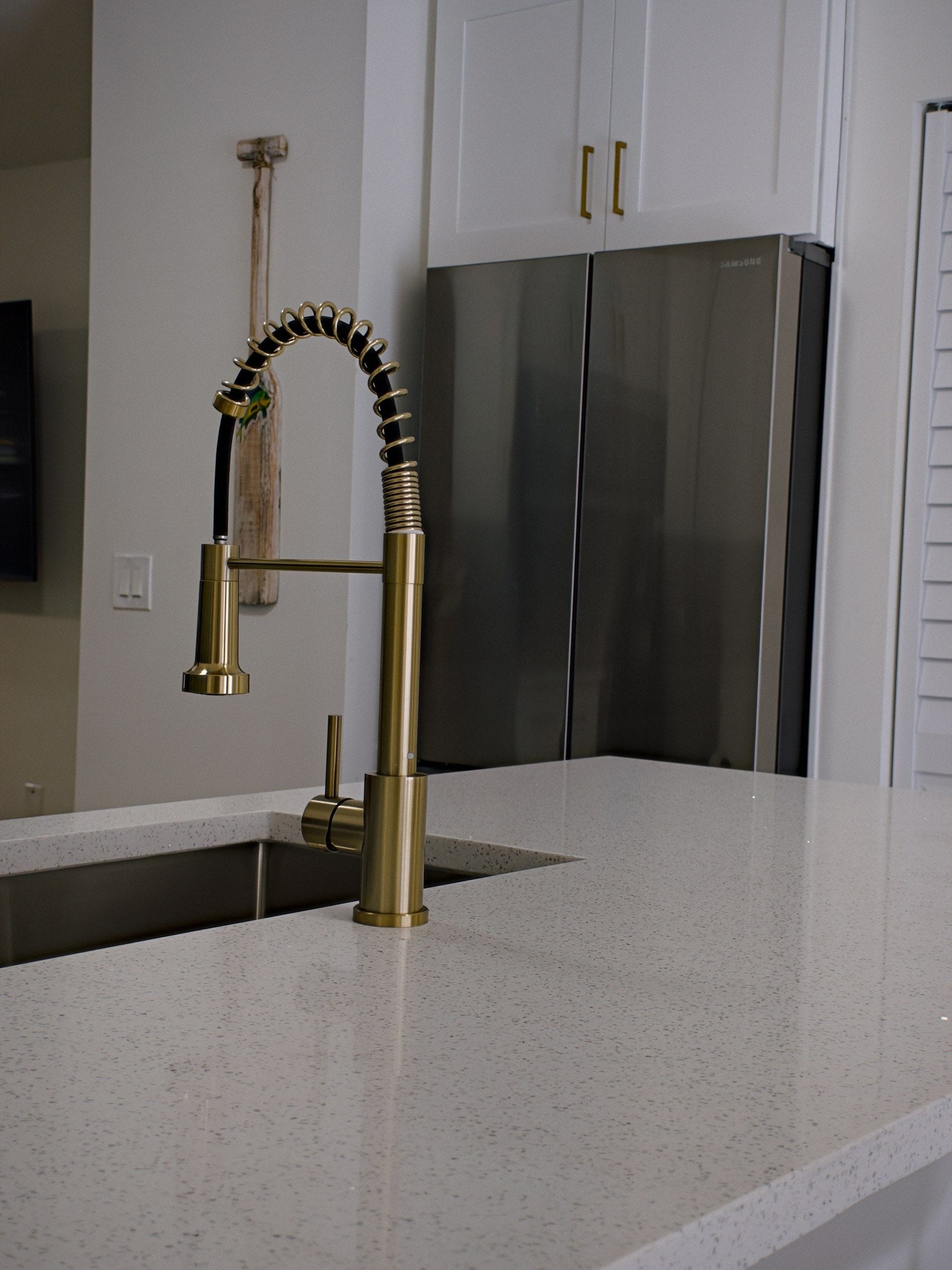 A kitchen with a stainless steel refrigerator, a gold faucet, and a white speckled countertop.
