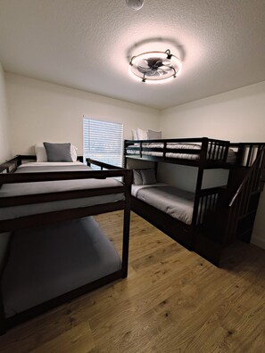 A bunk bed room with a ceiling fan, wooden flooring, and a window with blinds. - The Sailfish (Stuart)