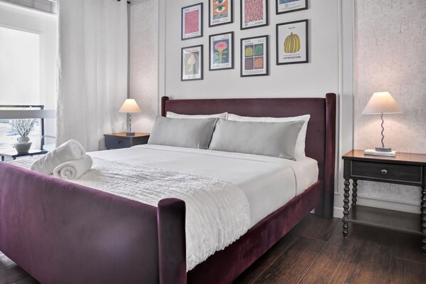 A neatly made bed with a white comforter and pillows, a wooden headboard, and a bedside table with a lamp. - Casa Positano® Designer 2BR/2BA in Irvine w/ Pool (Irvine)