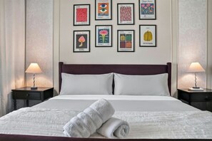 A neatly made bed with a white duvet and pillows, a rolled towel on the bed, and a series of framed botanical prints on the wall. - Casa Positano® Designer 2BR/2BA in Irvine w/ Pool (Irvine)