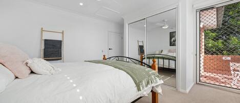 A bedroom with a bed, a mirror, a door leading to a balcony, and a ceiling fan.