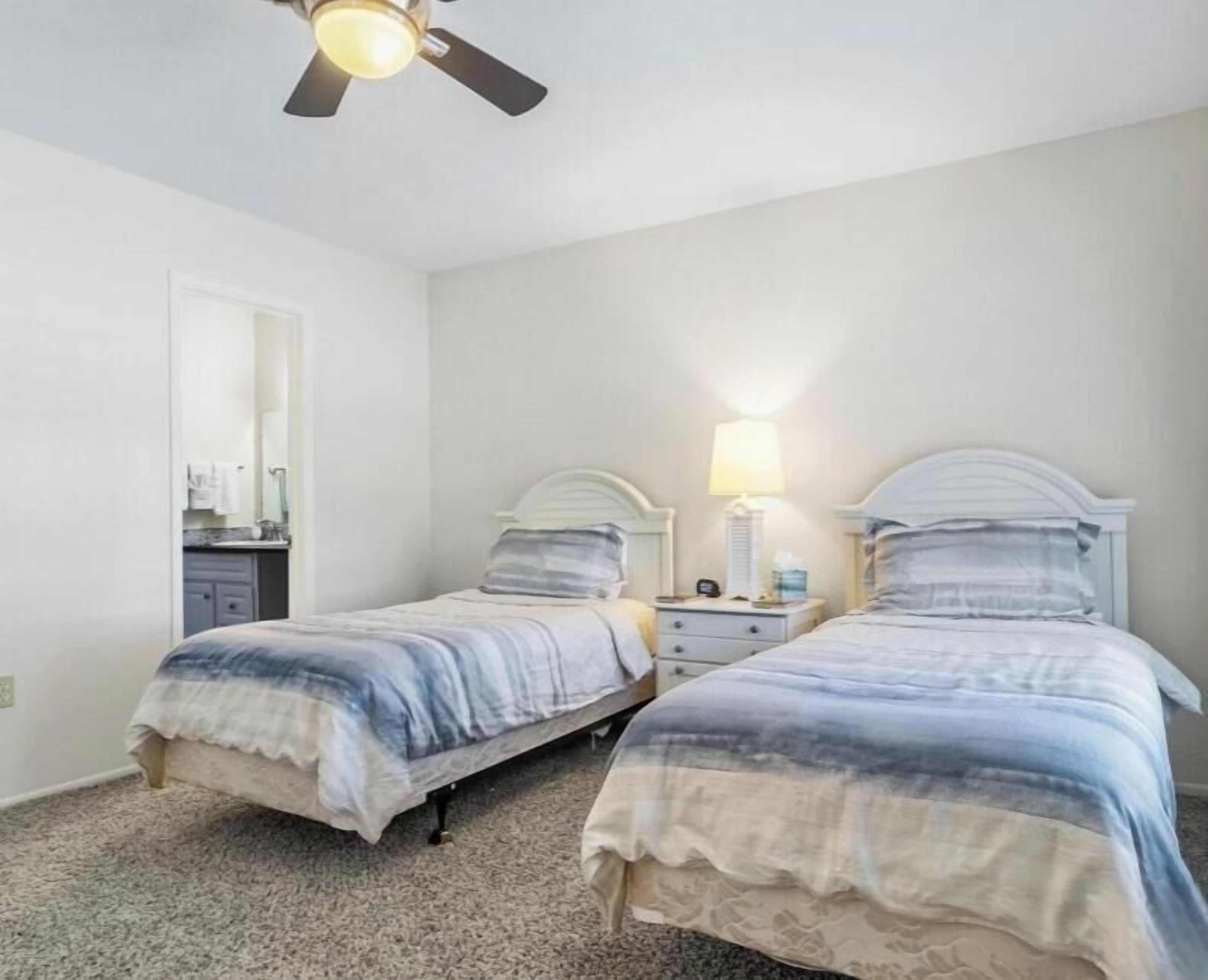 A bedroom with two beds, a ceiling fan, and a nightstand with a lamp.