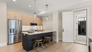 Cozinha moderna com eletrodomésticos de aço inoxidável, uma ilha central com banquetas e iluminação pendente.