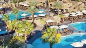 A resort with multiple swimming pools, palm trees, and a mountainous backdrop.