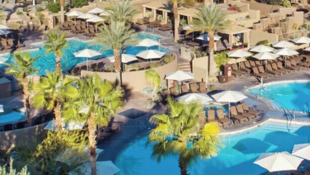 Ein Resort mit mehreren Schwimmbecken, Palmen und einer Bergkulisse.