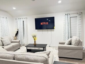 Ett modernt vardagsrum med en platt-TV som är monterad på väggen, två soffor, ett soffbord och dekorativa vaser.