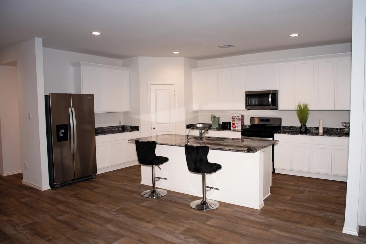 A modern kitchen with white cabinets, a stainless steel refrigerator, a microwave, and two black bar stools.