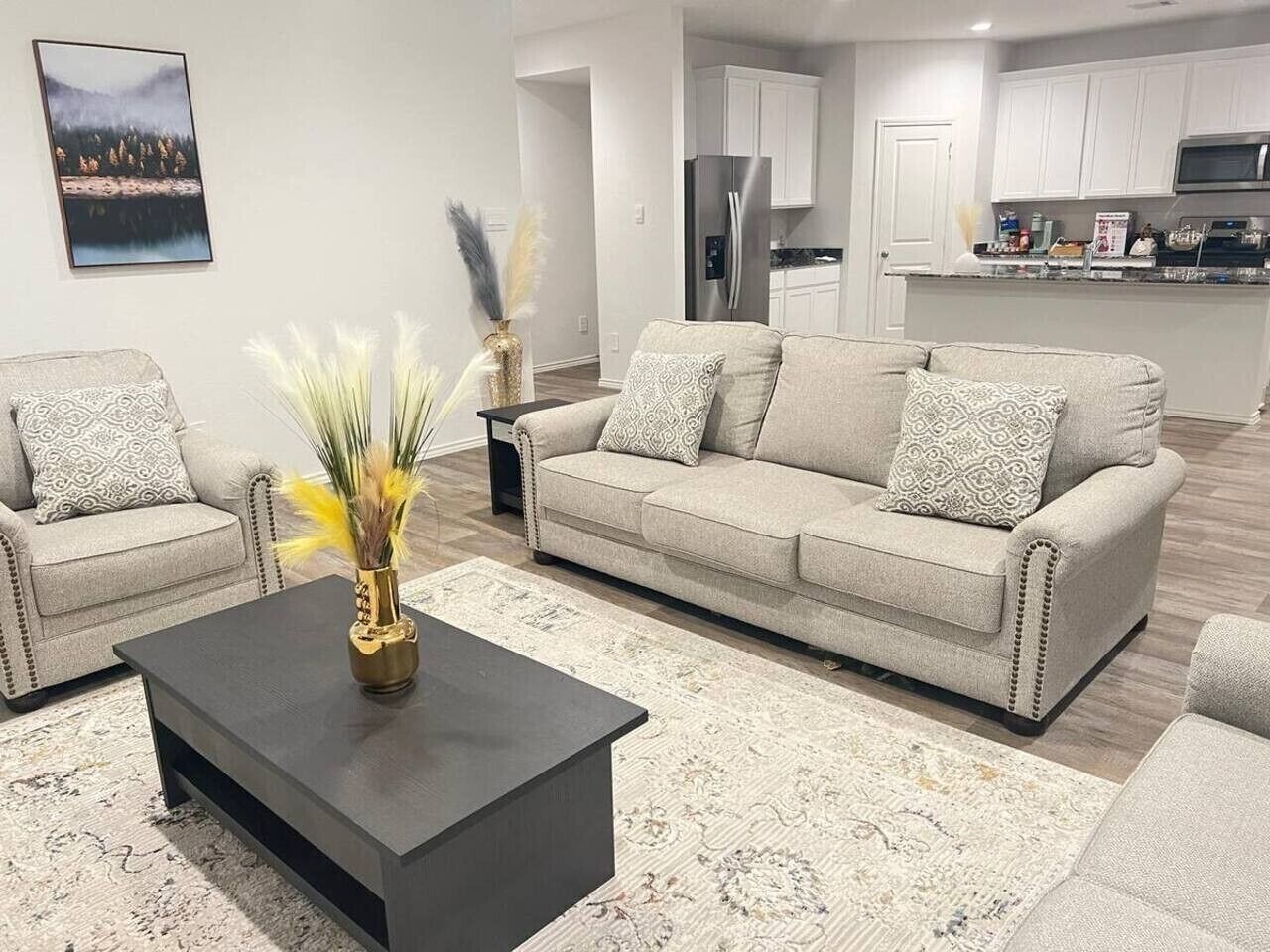 A modern living room with a sofa, armchairs, a coffee table, and a kitchen in the background.