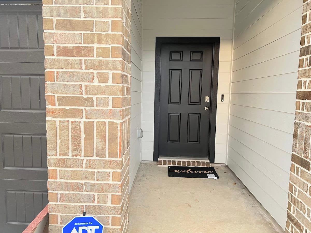 A garage entrance with a brick wall, a black door, and a welcome mat.