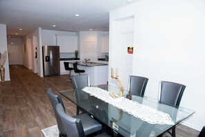 A modern kitchen with white cabinets, a stainless steel refrigerator, and a dining area with a glass table and chairs. - 5BR All One Level | Fenced Yard | Pet Friendly (Richmond)