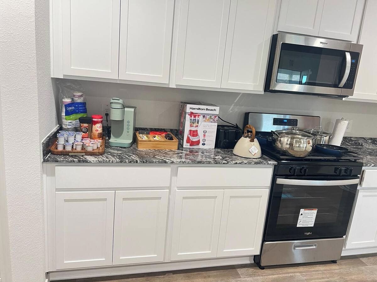 A kitchen with white cabinets, a microwave, a stove, and various kitchen items on the counter.