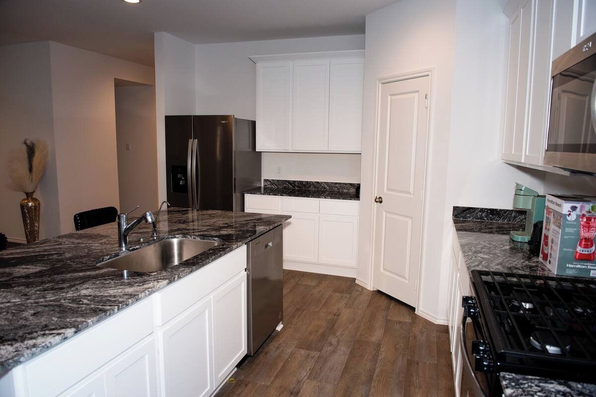 A modern kitchen with white cabinets, a stainless steel refrigerator, a dishwasher, and a gas stove.