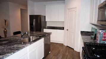 A modern kitchen with white cabinets, a stainless steel refrigerator, a dishwasher, and a gas stove.