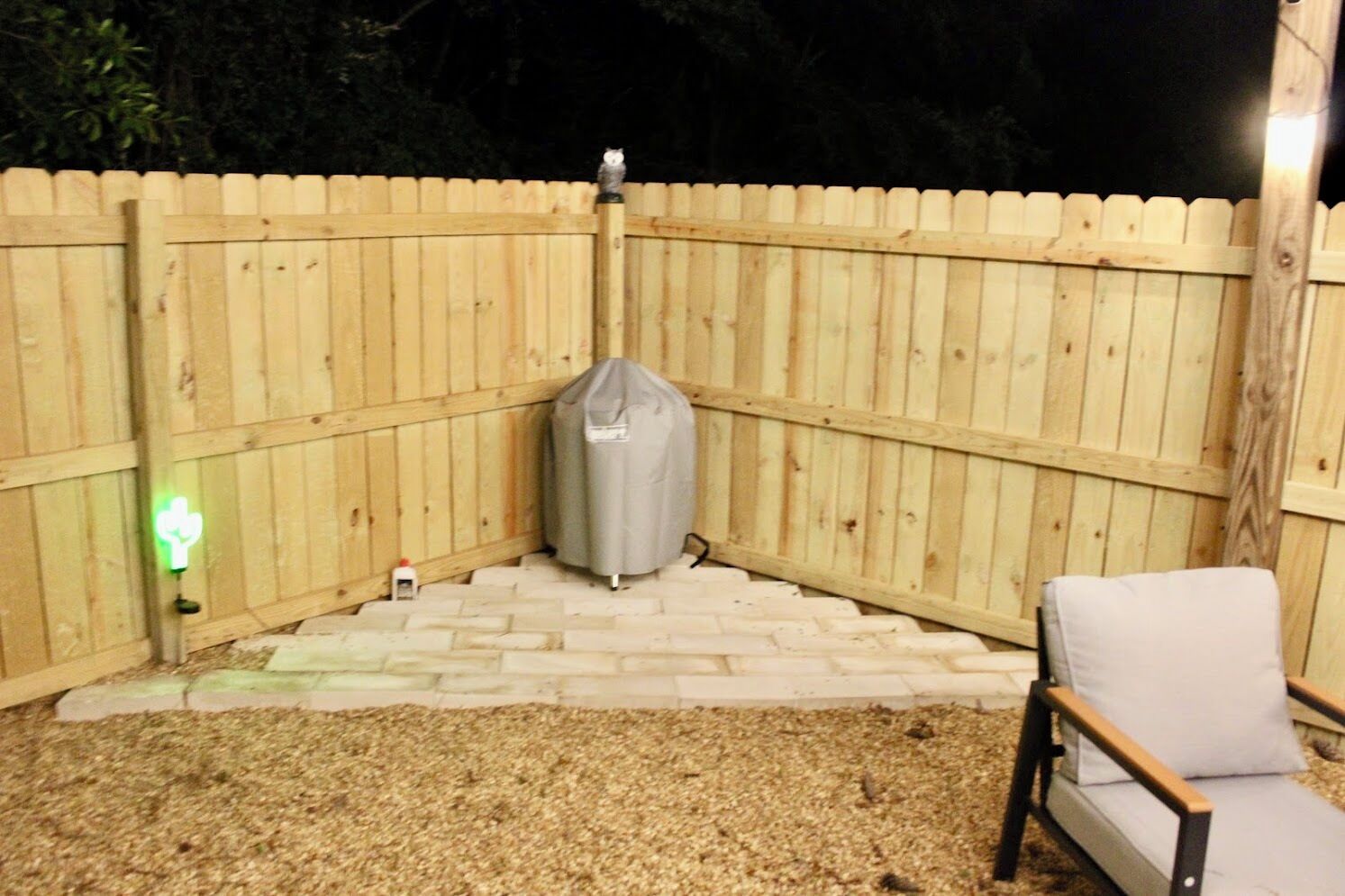 A fenced outdoor area with a covered grill, a chair, and a small table.