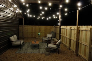 Um pátio externo com luzes de Natal, uma mesa, cadeiras e um cercado de madeira.