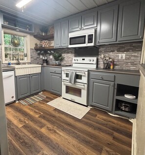 A kitchen with grey cabinets, a white stove, a microwave, and a wooden floor. - Enjoyable 2-bedroom building with AC for a relaxing stay (Morton)