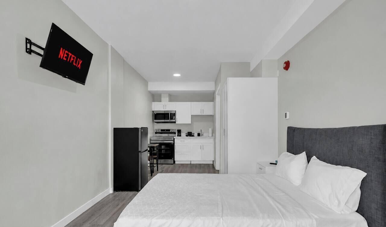 Ein stilvolles Hotelzimmer mit Bett, Flachbildfernseher an der Wand, einer Küchenzeile und einem separaten Badezimmer.