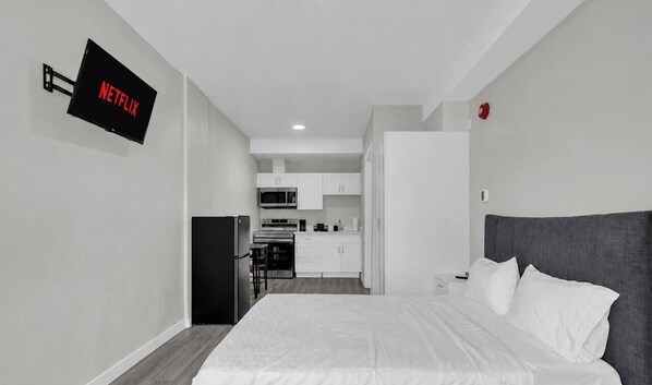 Ein stilvolles Hotelzimmer mit Bett, Flachbildfernseher an der Wand, einer Küchenzeile und einem separaten Badezimmer.