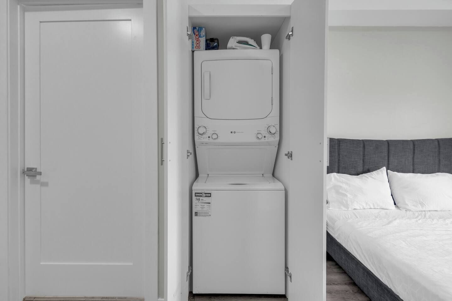Une petite pièce comprenant un lit, un lave-linge et une porte.