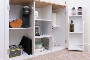A white storage unit with shelves containing a coffee maker, a toaster, and various containers.