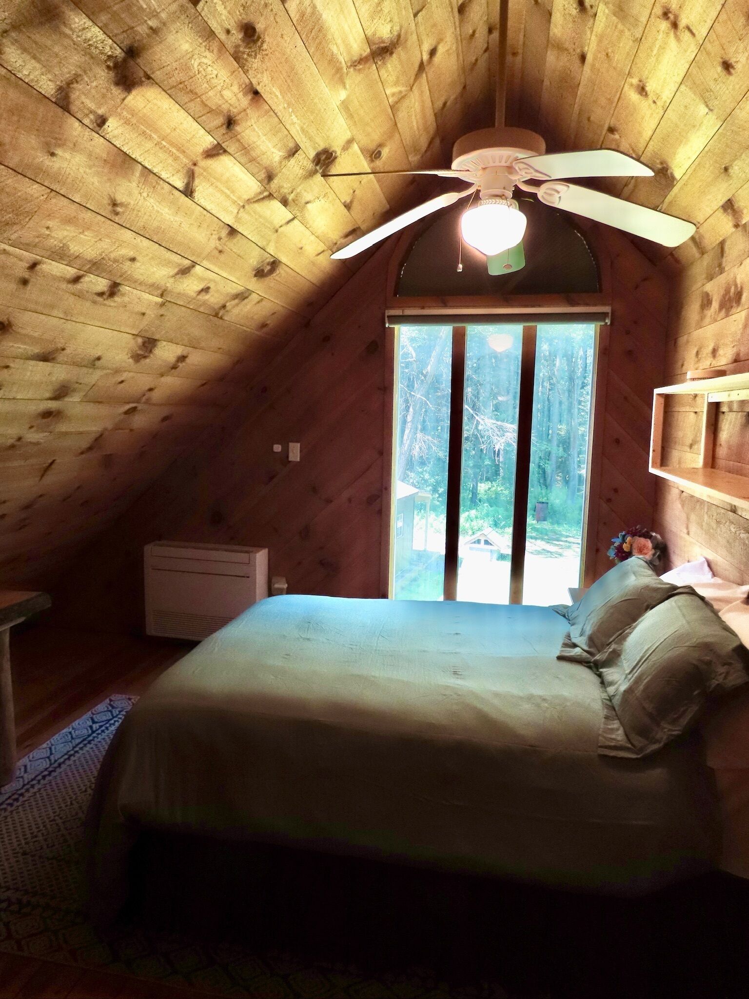 A bedroom with a sloped ceiling, a bed, a nightstand, a window, and a ceiling fan.