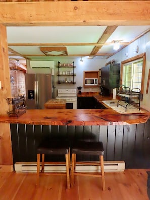 A kitchen with a wooden countertop, a stove, a microwave, and a sink. There are two stools and a window with a view.